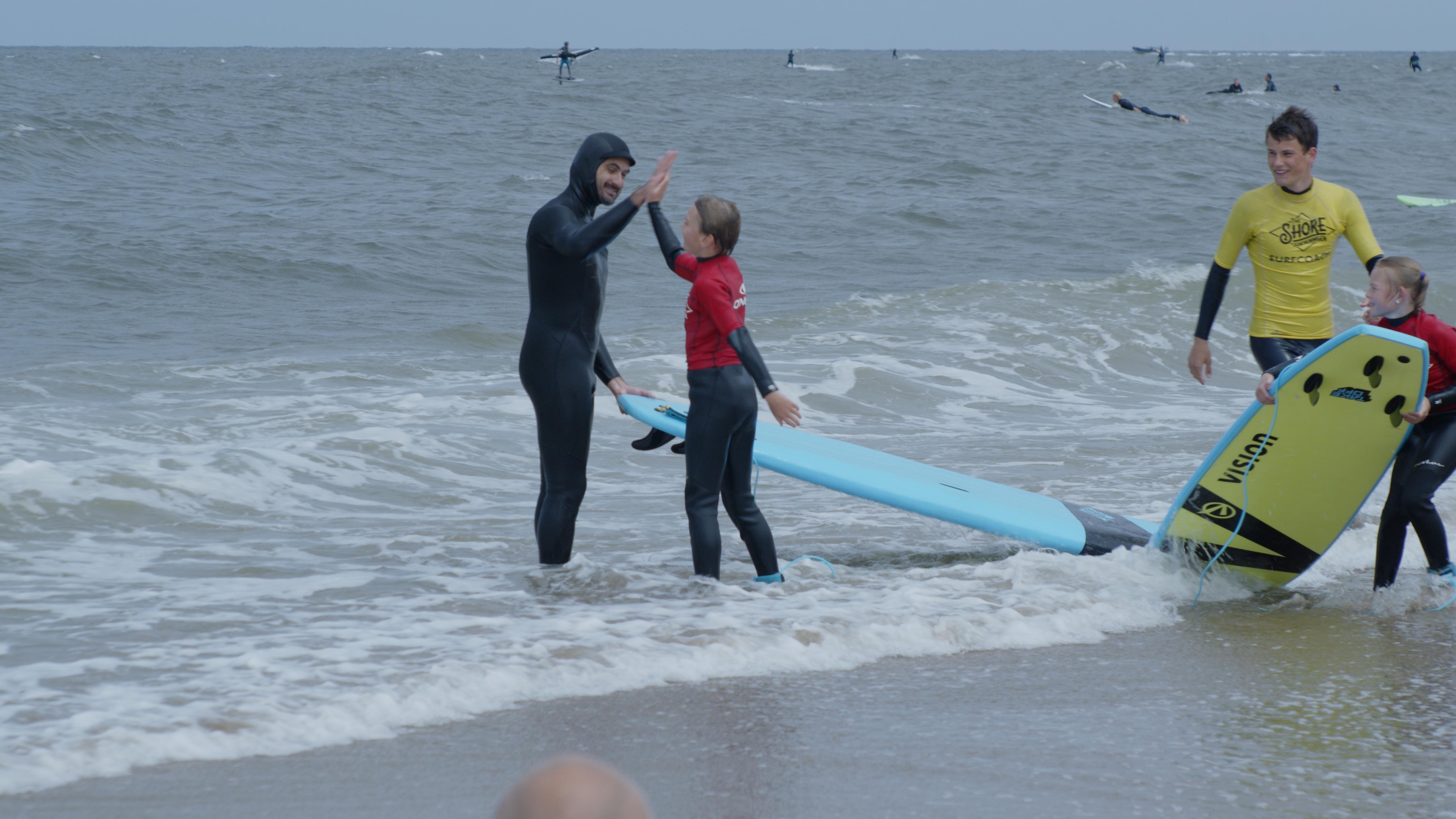 Sacha peddelt op zijn surfboard de golven in.